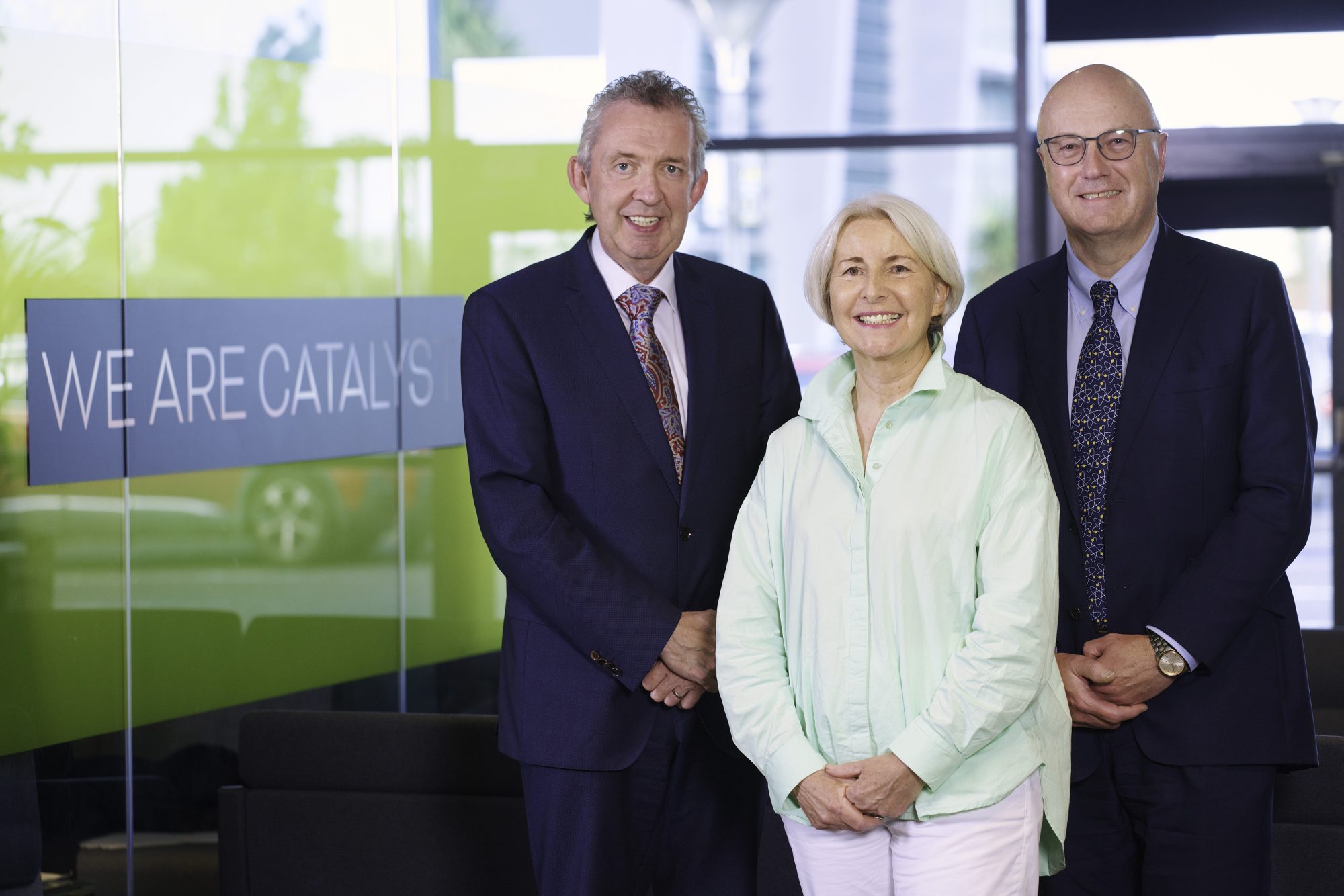 A picture of Catalyst's three new board members (Professor Mark W.J Ferguson, Jeanette Walker and Paul Harrington) standing together next to a branded, glass wall.